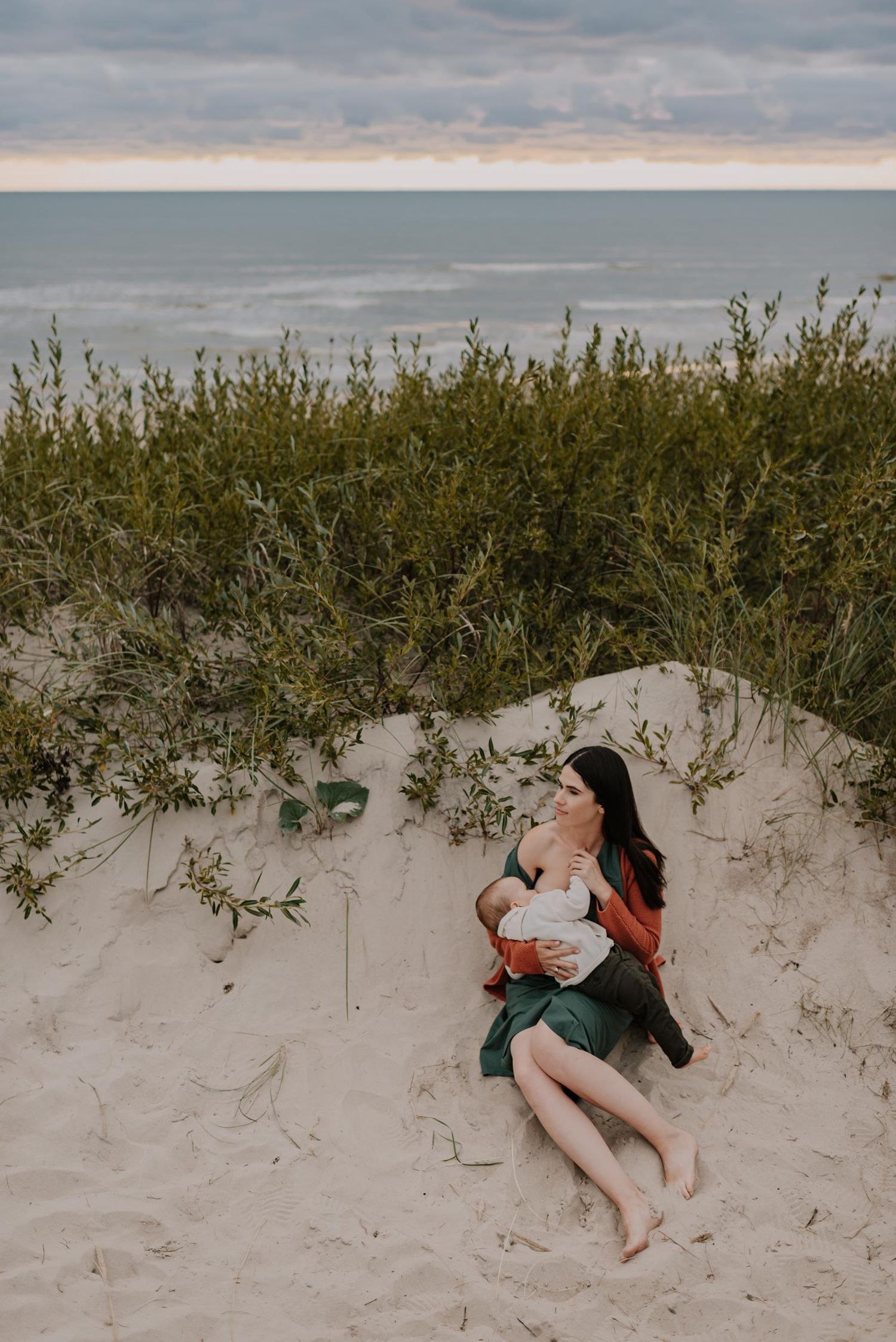 Family relaxing together in beach sand dunes during overcast day.