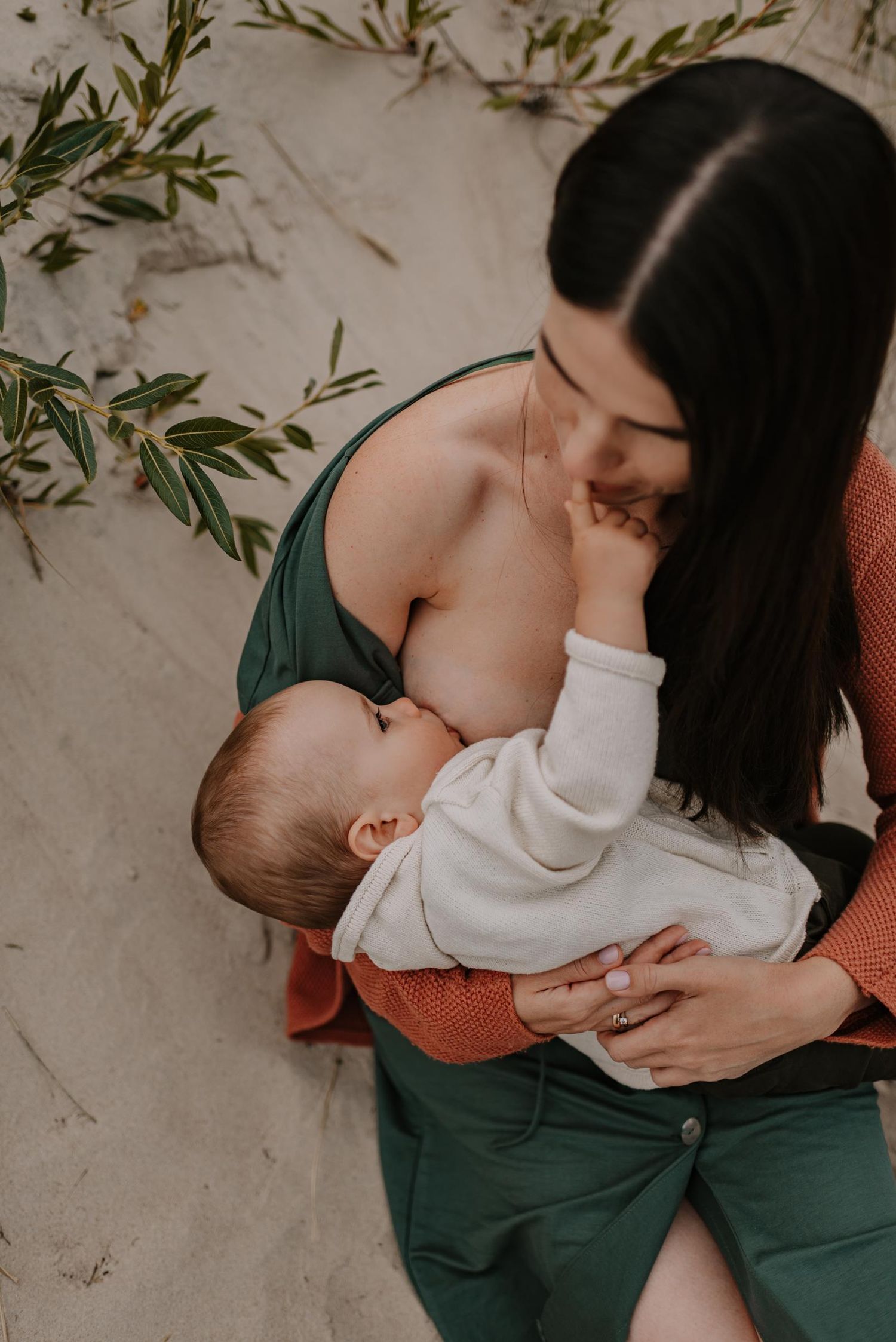 Tender and intimate moment of nursing a baby on sandy beach with natural beach grass in background.