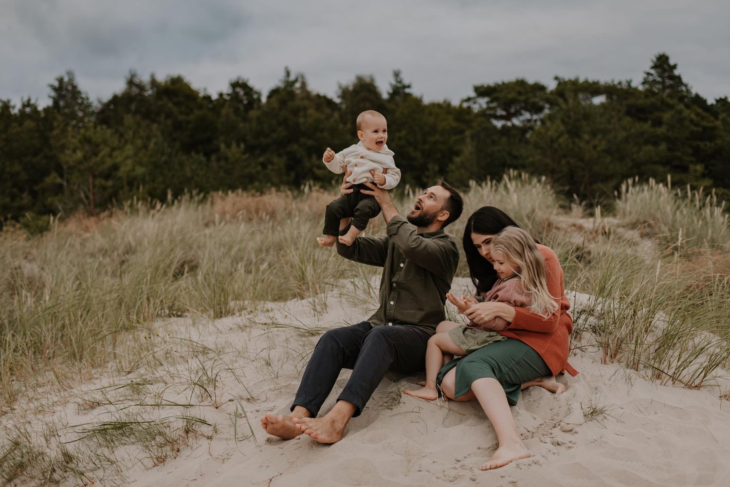 Natural lifestyle portrait of family sitting together among beach dunes.