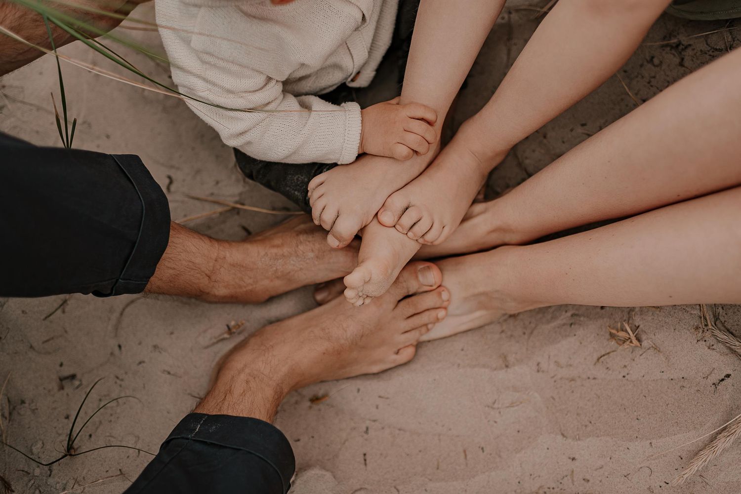 Close up detail of bare feet and hands in sand during beach family photo session.
