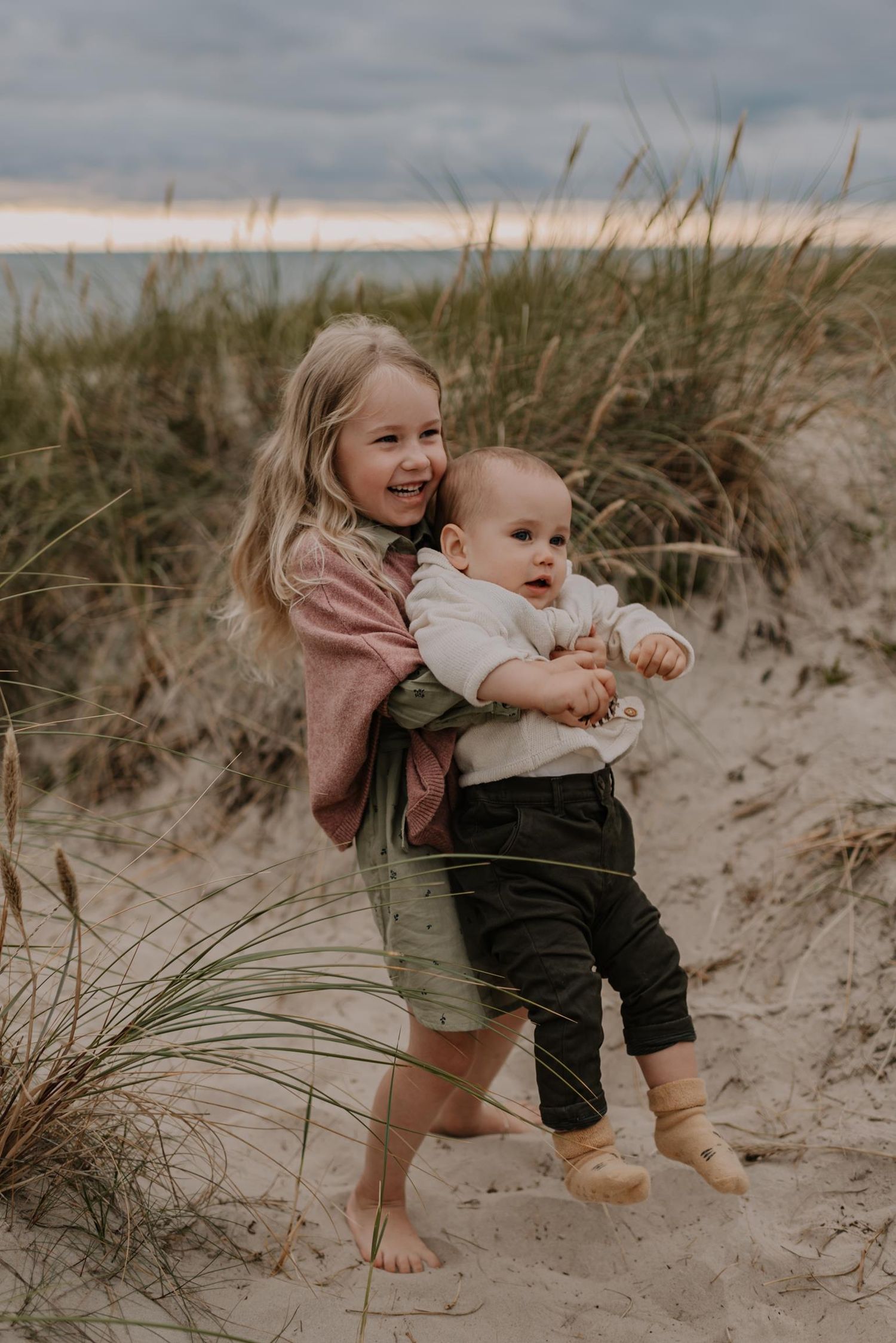 Siblings playing and exploring together in sand dunes at beach.