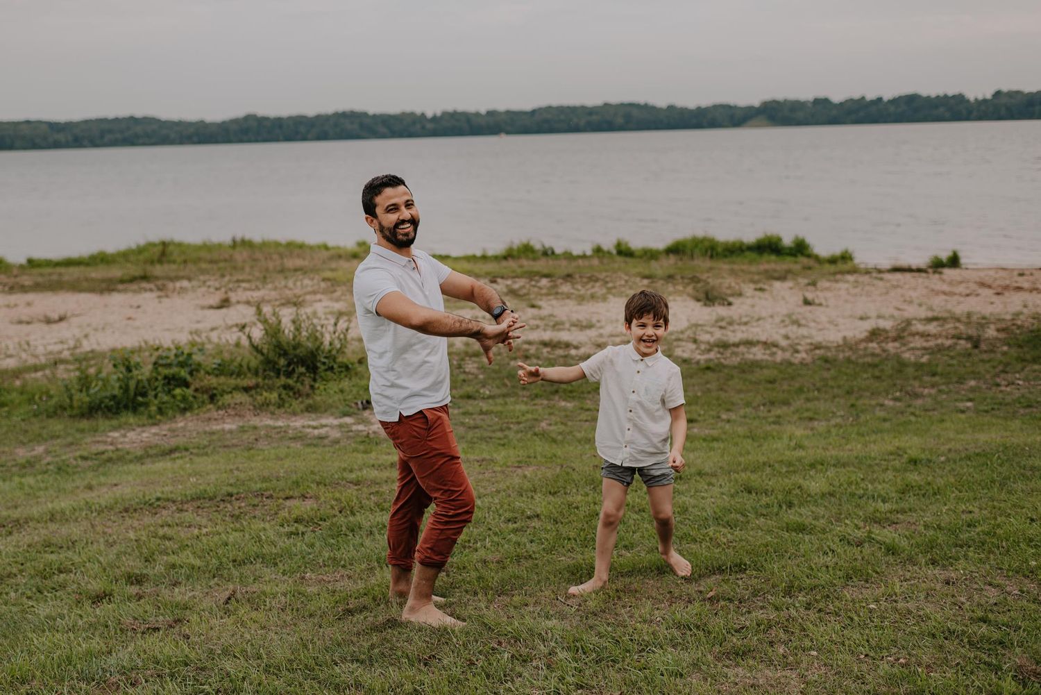 Two people playing and dancing together on grassy waterfront area.