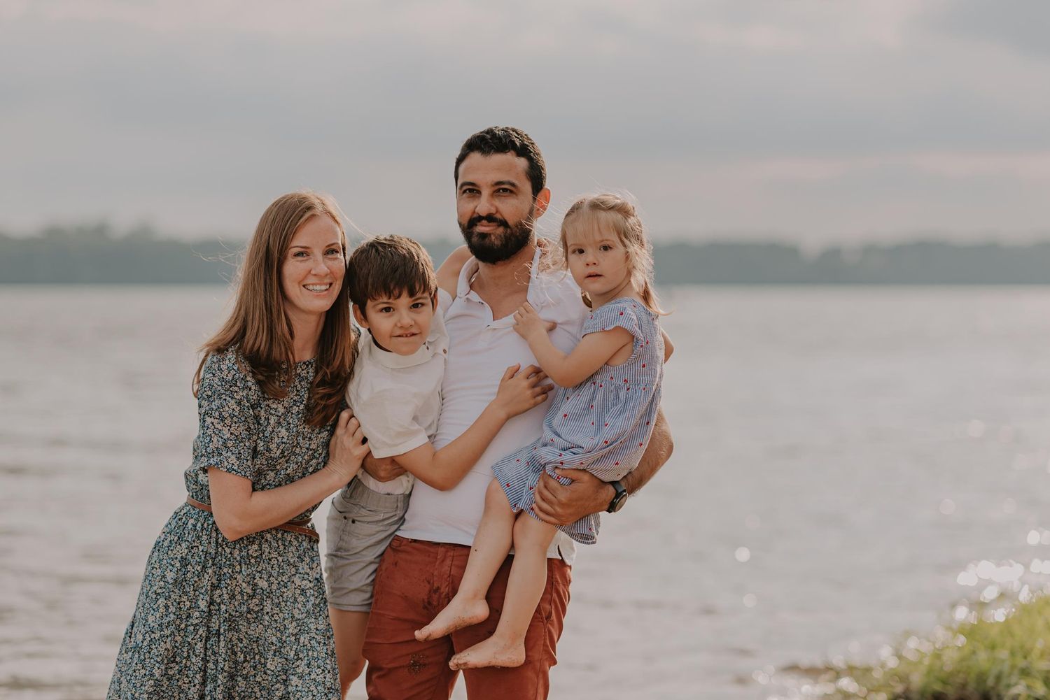 Happy family of four posing together on a beach at sunset.
