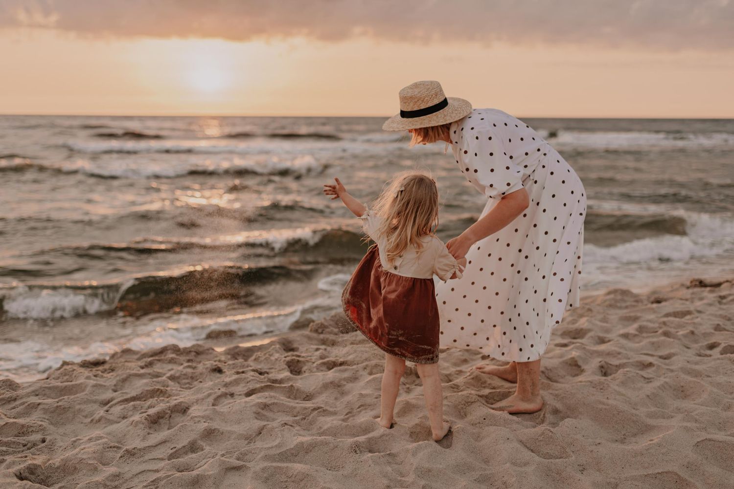 Couple embraces on sandy beach during golden sunset with waves crashing in background.