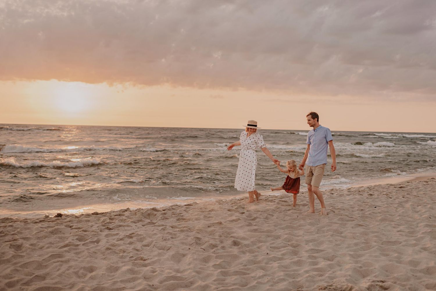 Family walking along sandy beach together during golden hour sunset.