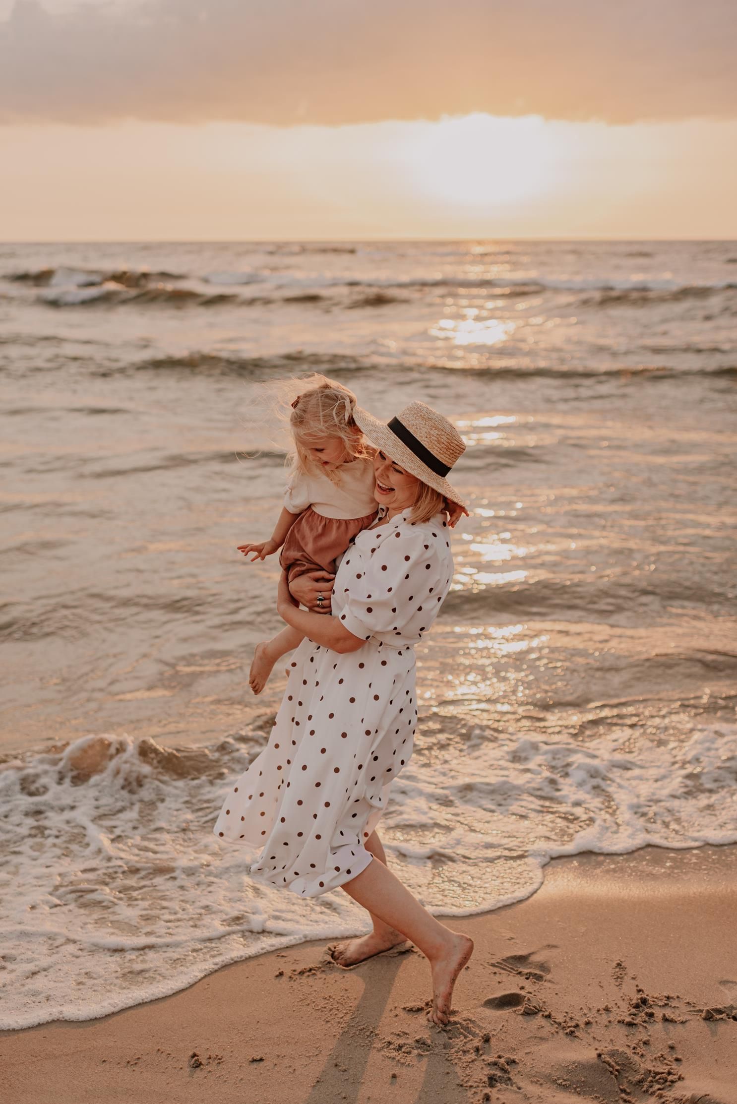 People playfully interact near ocean waves during golden hour sunset.