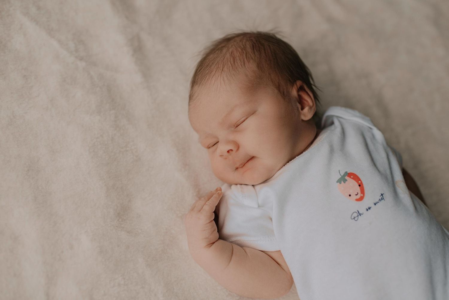 Sleeping newborn wearing white clothing laying on soft bedding.