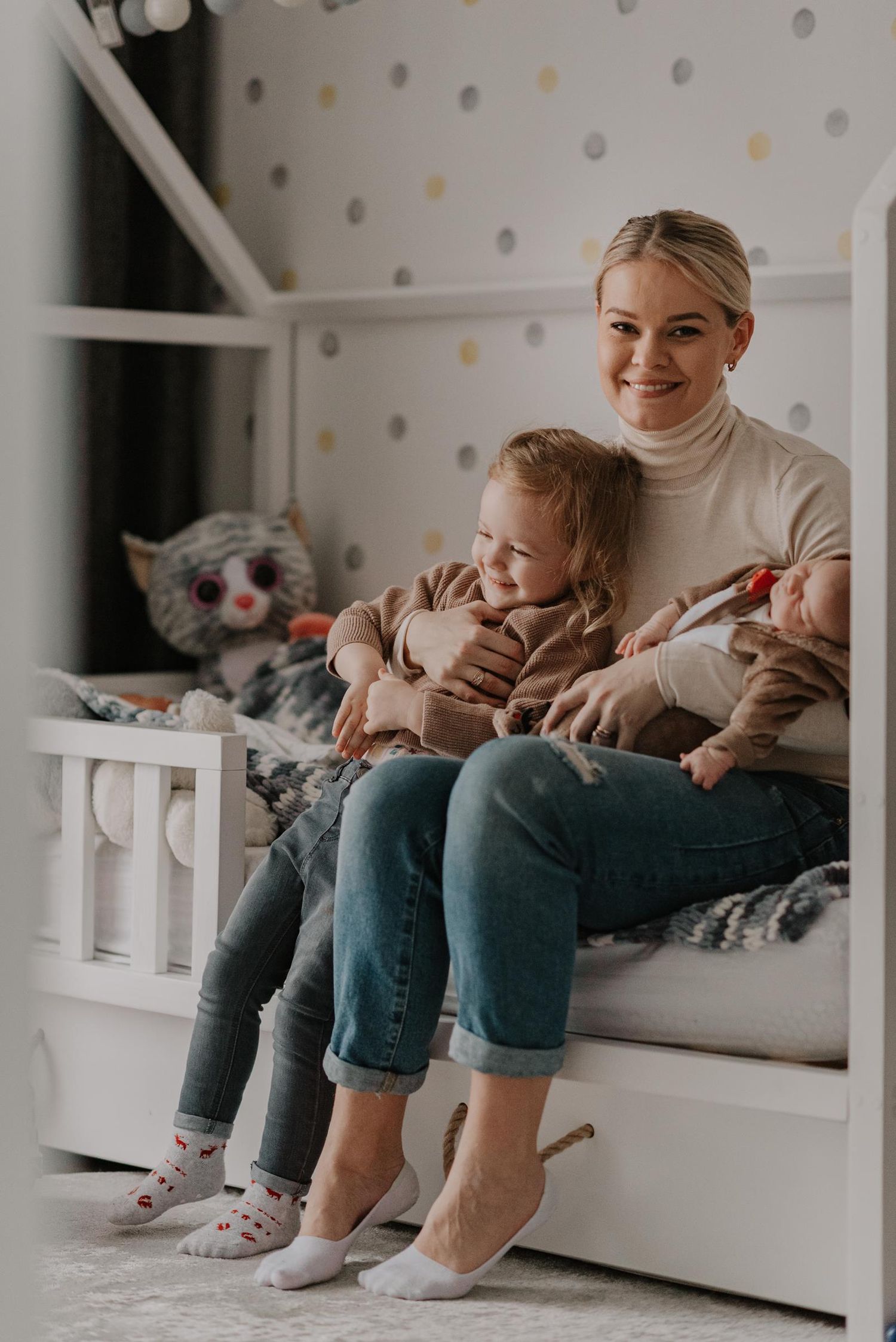 Family sitting together on white couch with polka dot wallpaper in background.