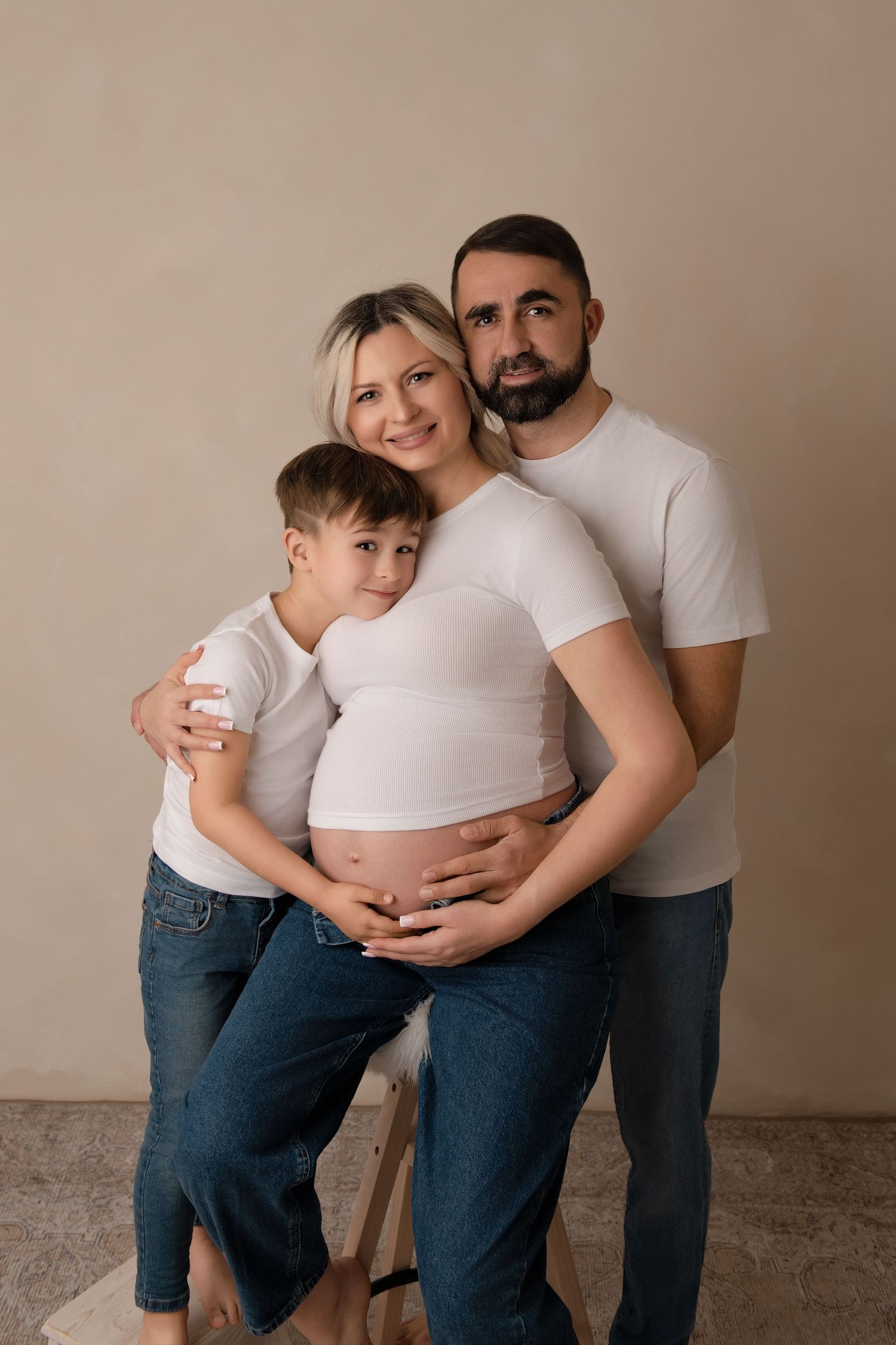 A maternity photo series showing a family embracing and celebrating pregnancy in matching white shirts and jeans.
