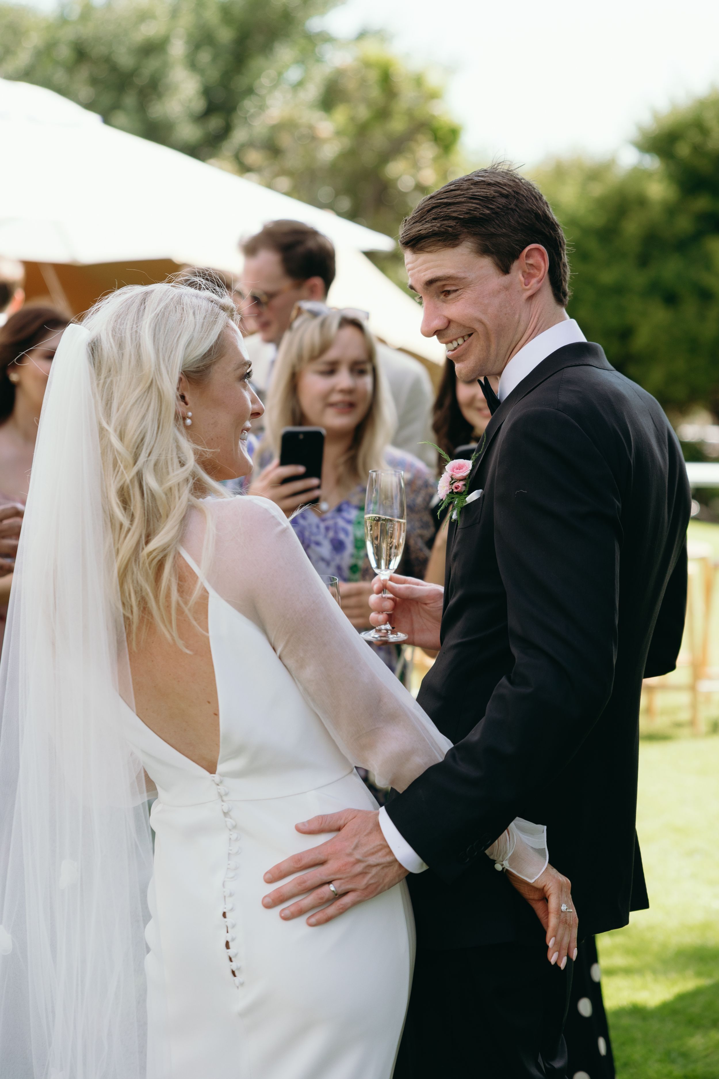 A candid moment at an outdoor wedding reception with guests enjoying champagne on a sunny day.