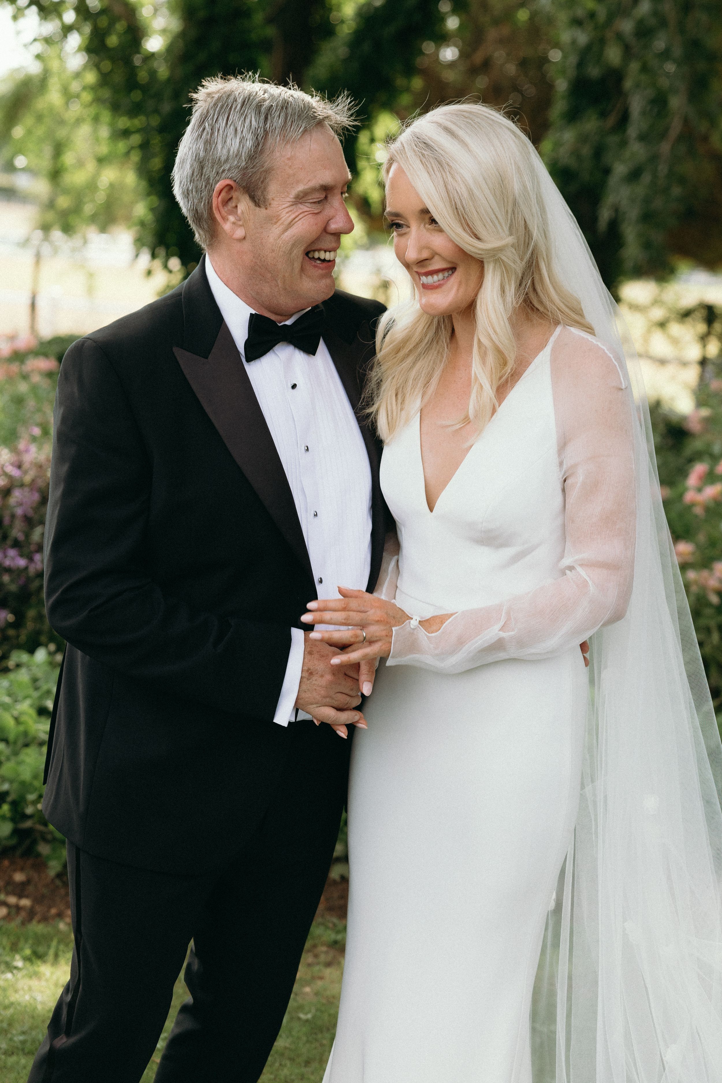 A bride and groom share an intimate moment in a garden setting while wearing formal wedding attire.