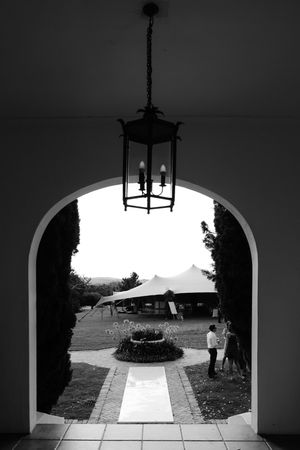 Four black and white arched doorways frame a garden path leading to an outdoor patio area with hanging light fixtures.