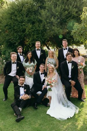 Wedding party in formal attire poses on grassy lawn during outdoor garden celebration.