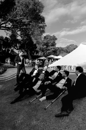 Wedding party members in formal attire lying on grass having fun during outdoor photo session.