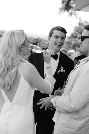 A series of black and white candid wedding photos showing joyful moments and laughter between guests at a celebration.