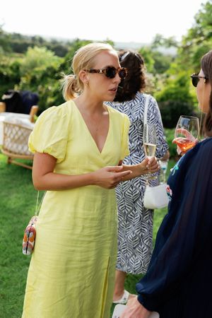 Wedding guests mingling at outdoor reception with drinks in hand on sunny day.