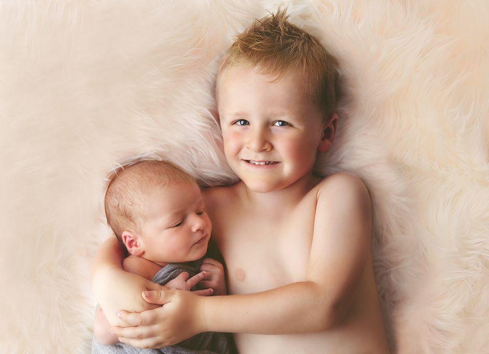Newborn baby wrapped in soft white fabric lying on cream-colored textured blanket during professional photo session.