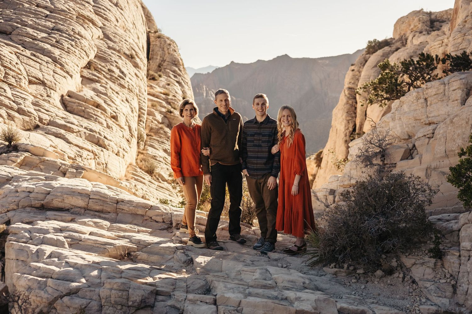 Group standing together on rocky terrain with towering canyon walls and mountains in the background.