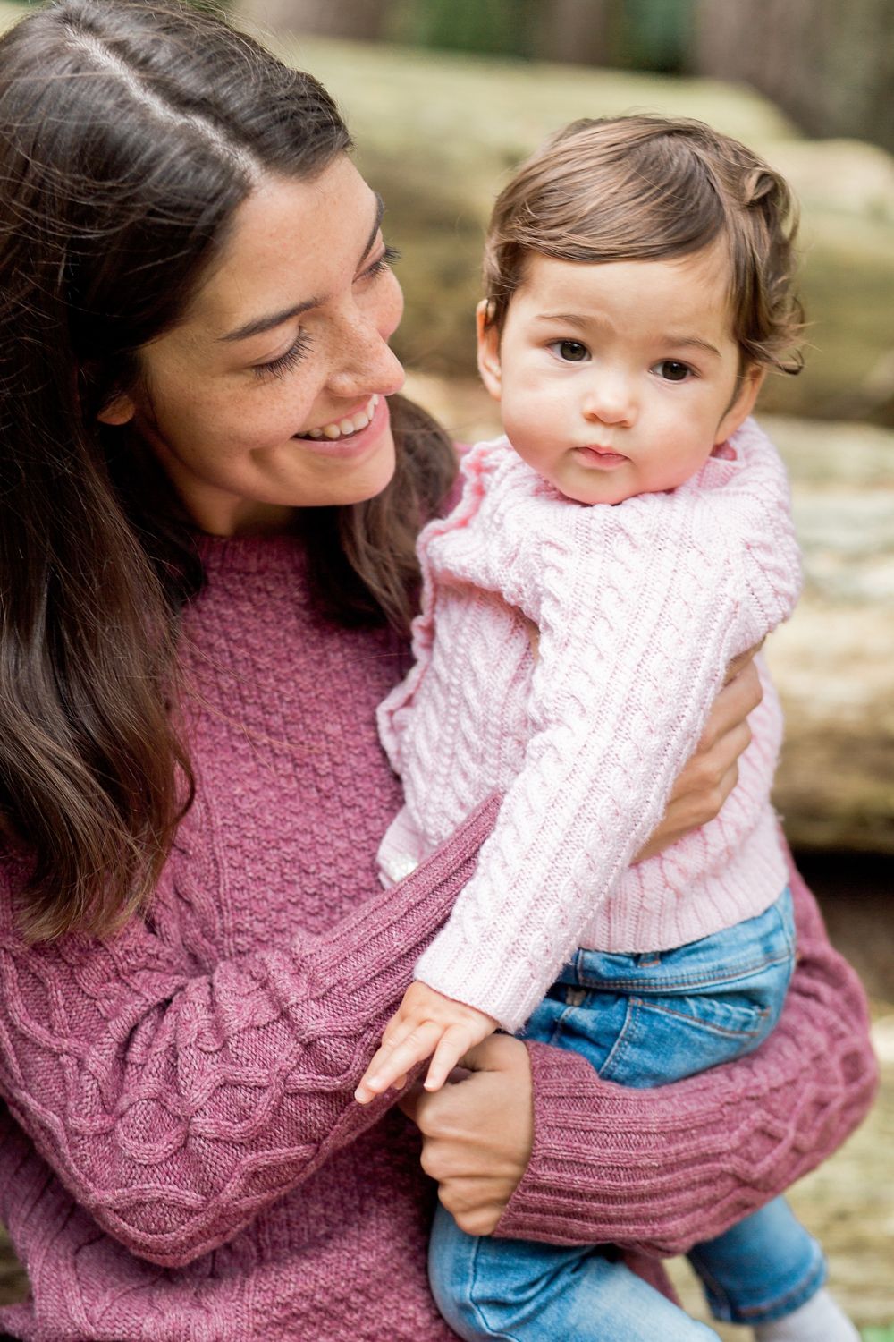 A parent in a mauve knit sweater shares tender moments with a baby wearing pink and denim in outdoor portraits.