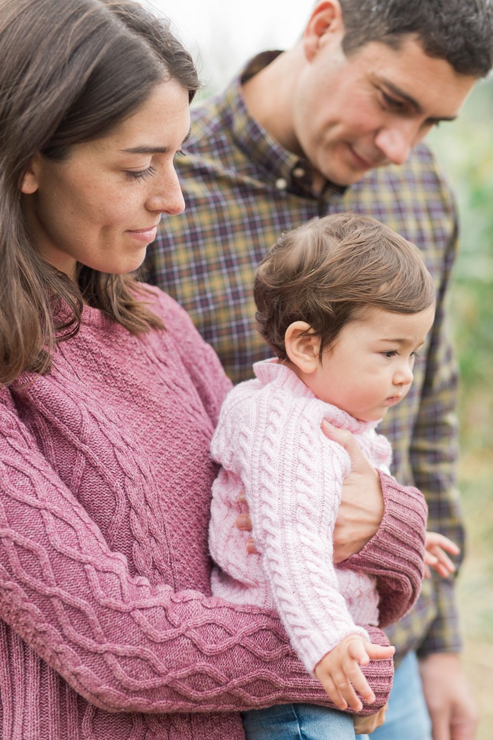 Family wearing cozy knit sweaters embrace in a tender outdoor autumn moment.