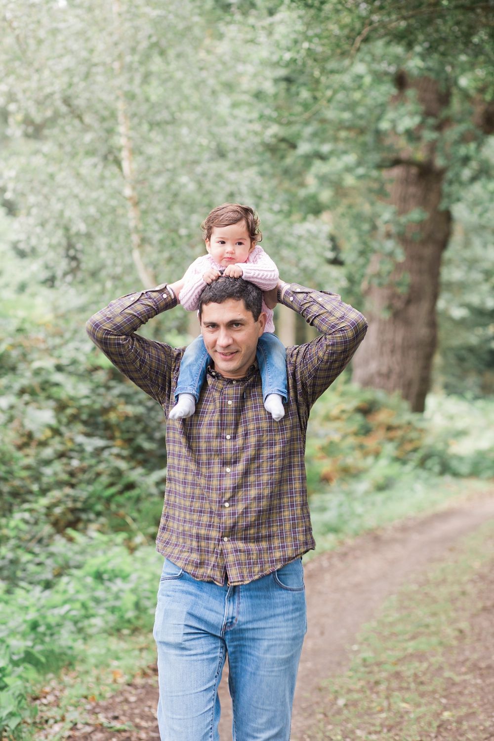 A person in a plaid shirt and jeans makes silly expressions while standing on a wooded trail.