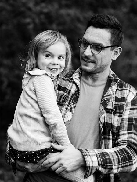A black and white portrait of an adult wearing glasses and plaid shirt holding a smiling young child in a sweater.