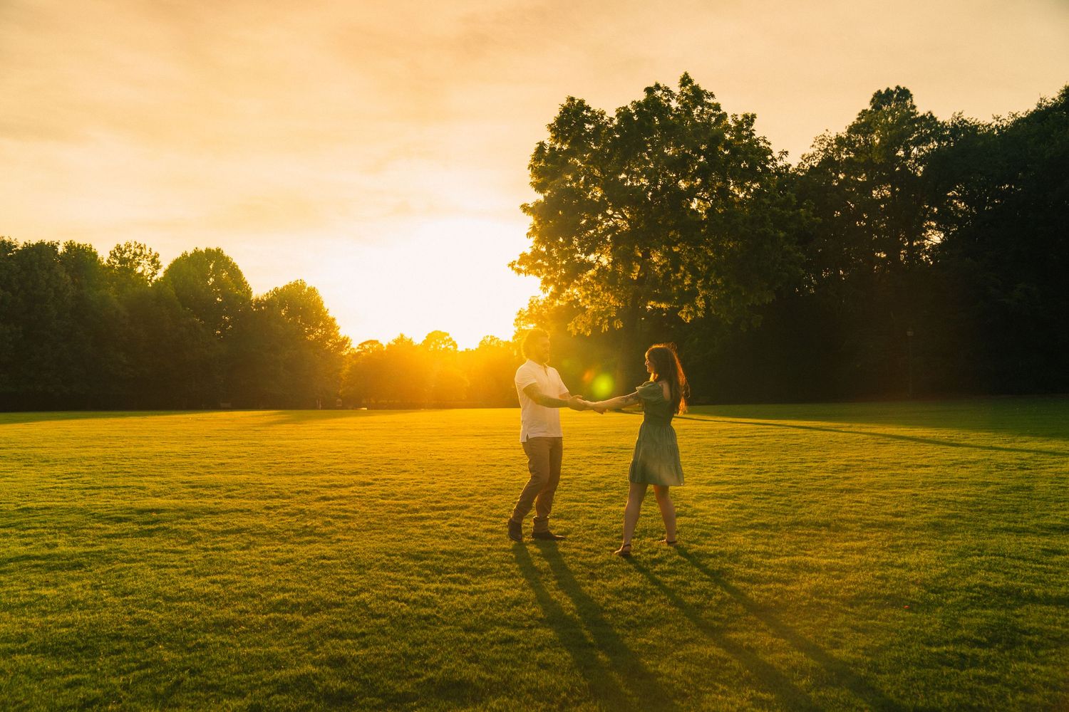 Two silhouettes walk together across a grassy field at sunset with golden light streaming through the trees.