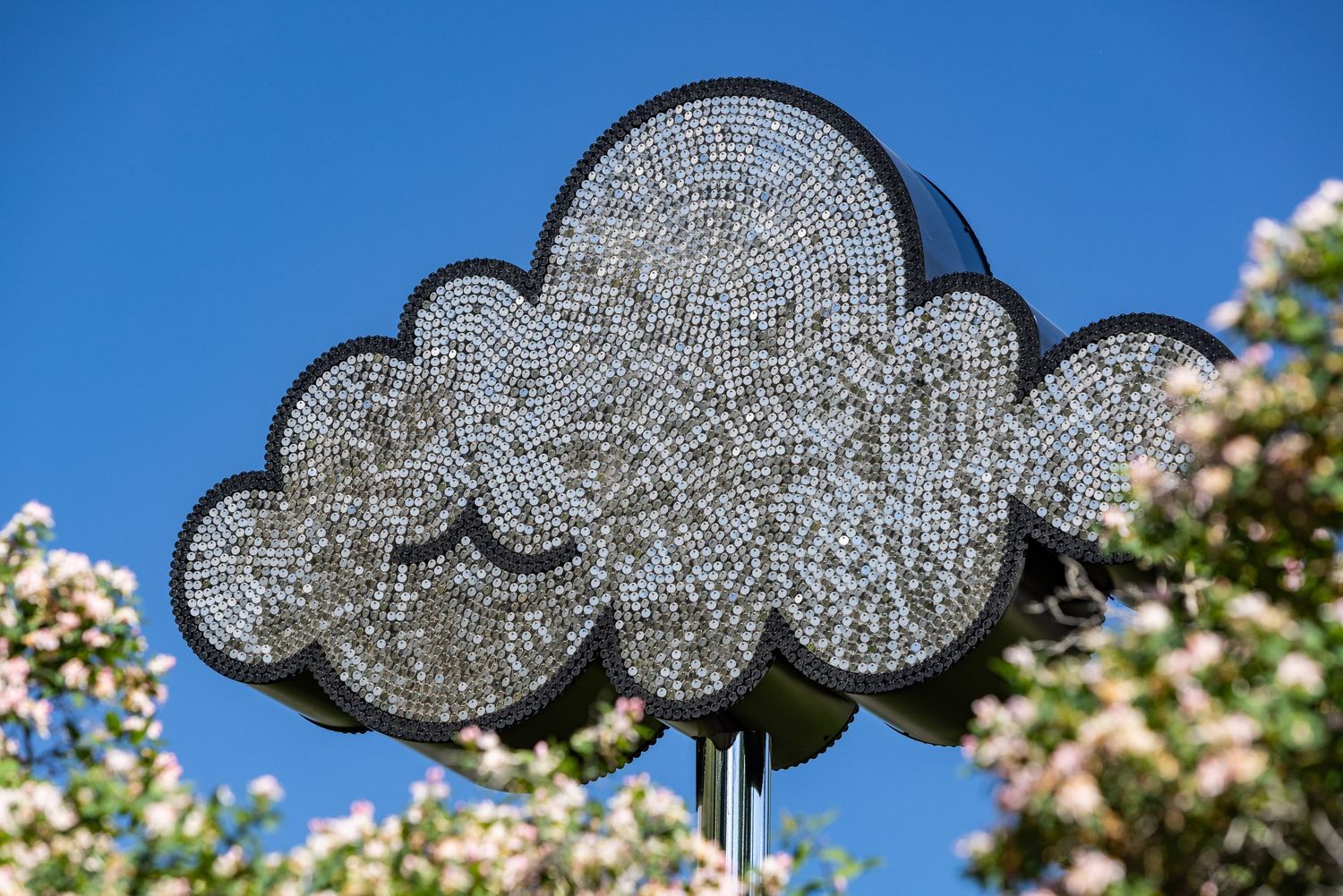 Glittery cloud-shaped decorations hang against a bright blue sky with white spring blossoms in the background.