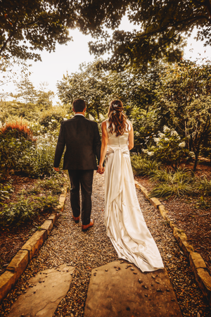 Wedding couple walking along a scenic garden path surrounded by lush greenery.