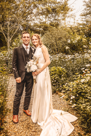 Bride in flowing dress and groom share intimate moments on garden path.