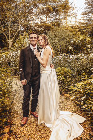 Wedding couple poses on a leaf-covered path during golden hour.