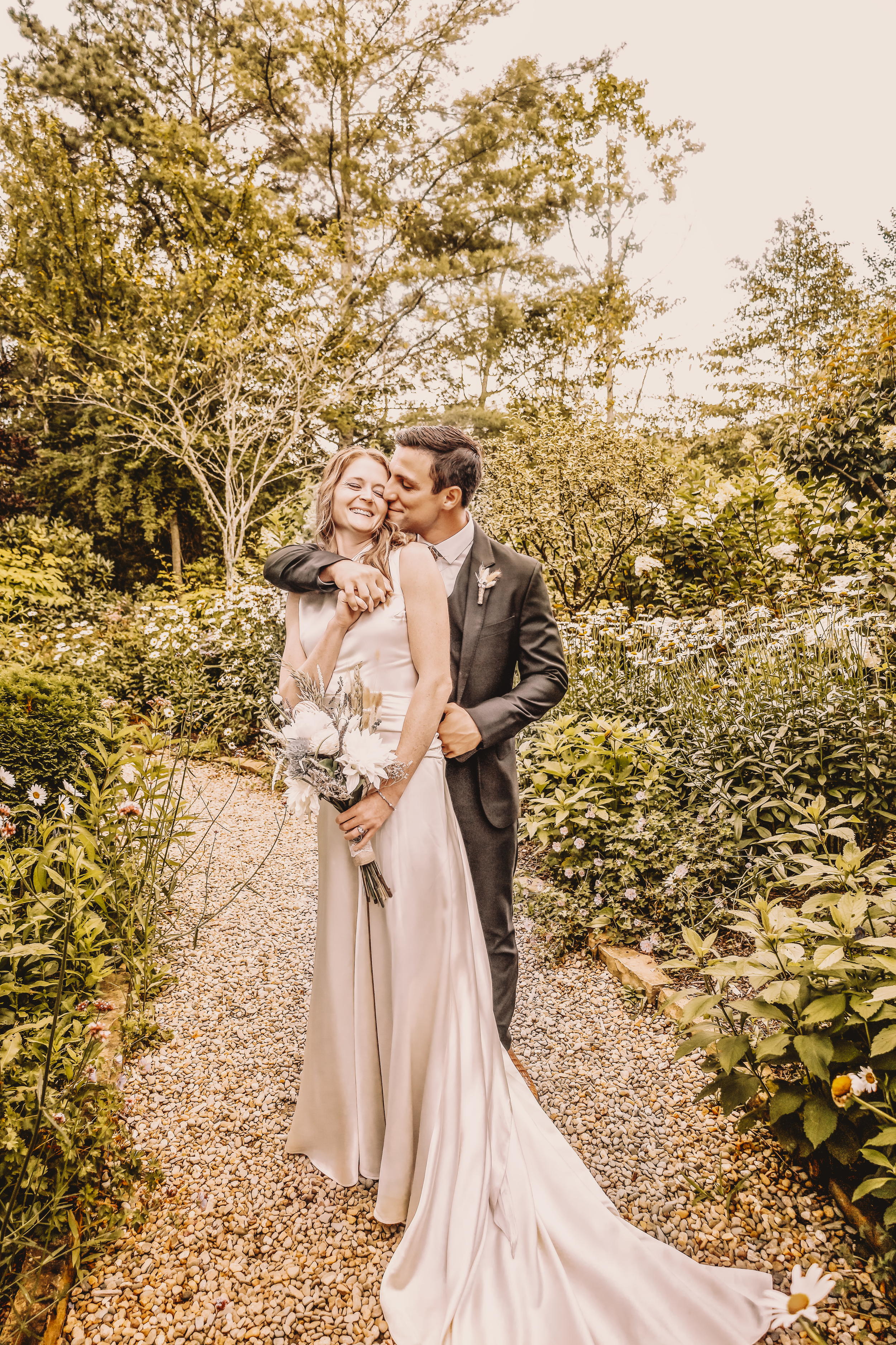 Sunset wedding photos of couple embracing on garden path with golden light.