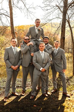 Wedding party in gray suits posing along a lake shore in fall scenery.