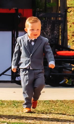 Small child in formal suit walking on grass during outdoor wedding.