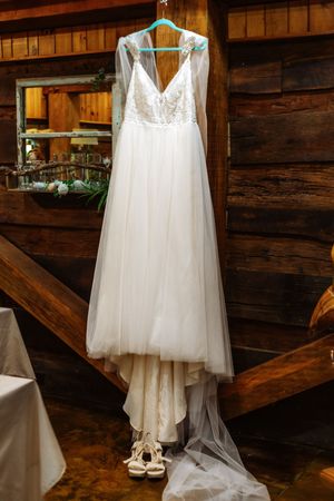 Elegant white wedding dress with lace bodice hanging in rustic wooden venue.