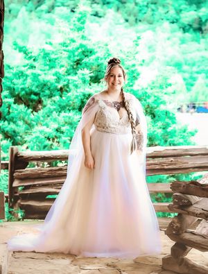 Bride in flowing white gown poses against vibrant green outdoor backdrop.