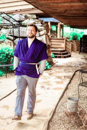 Person in purple wrap top and gray pants standing on rustic porch.
