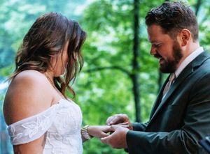 Wedding couple exchanges rings during their ceremony in front of a scenic waterfall.