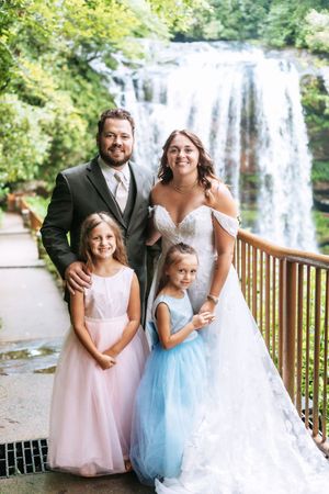 Wedding party photos featuring flower girls in pastel dresses posing near a waterfall.