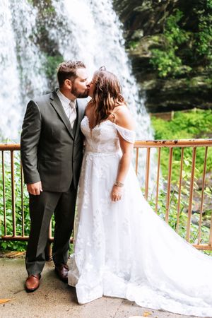 A romantic wedding photo series showing a couple posing by a cascading waterfall with a wooden railing.