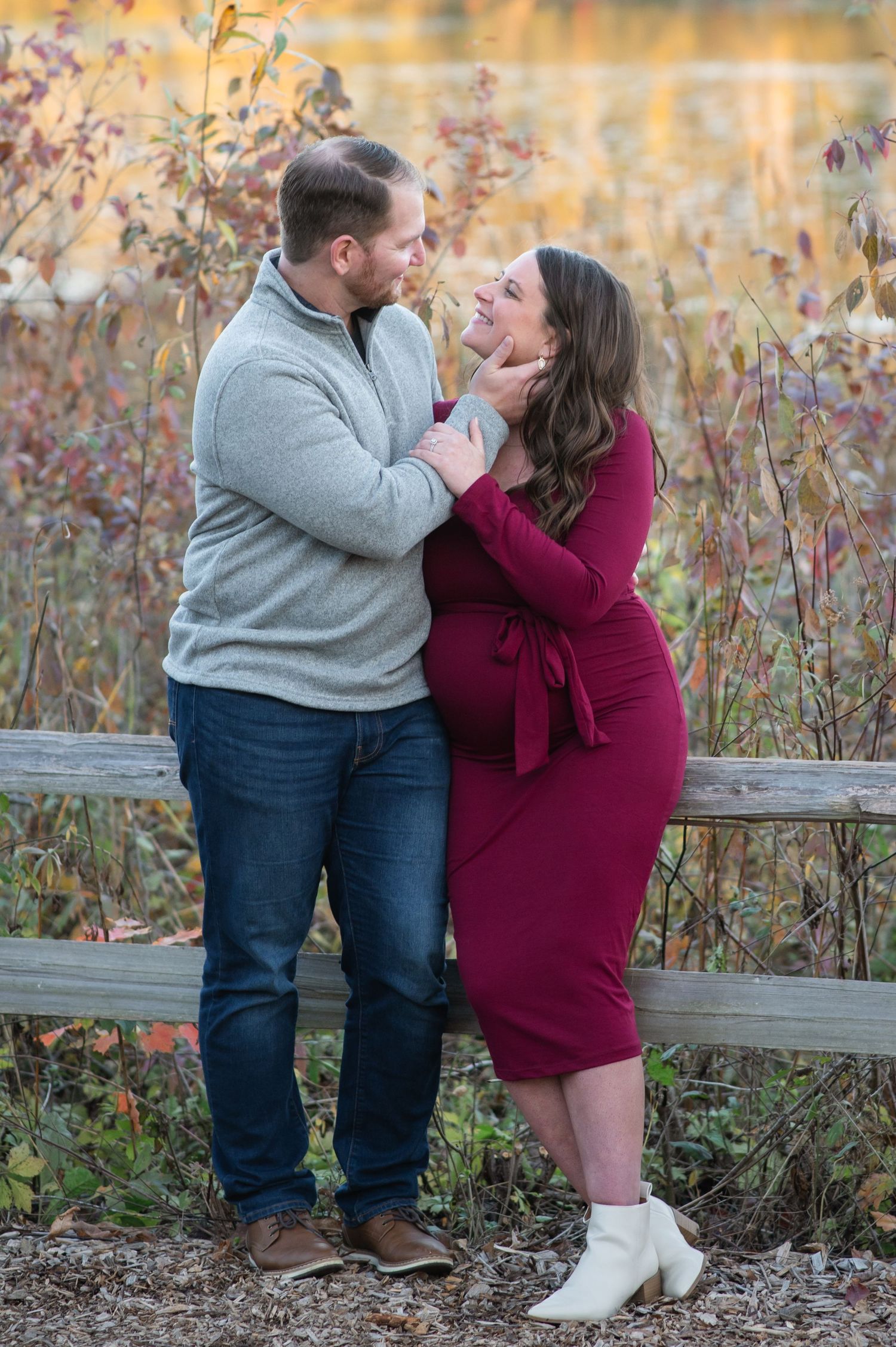 A couple in casual attire shares romantic moments by a rustic wooden fence during an autumn outdoor photoshoot.