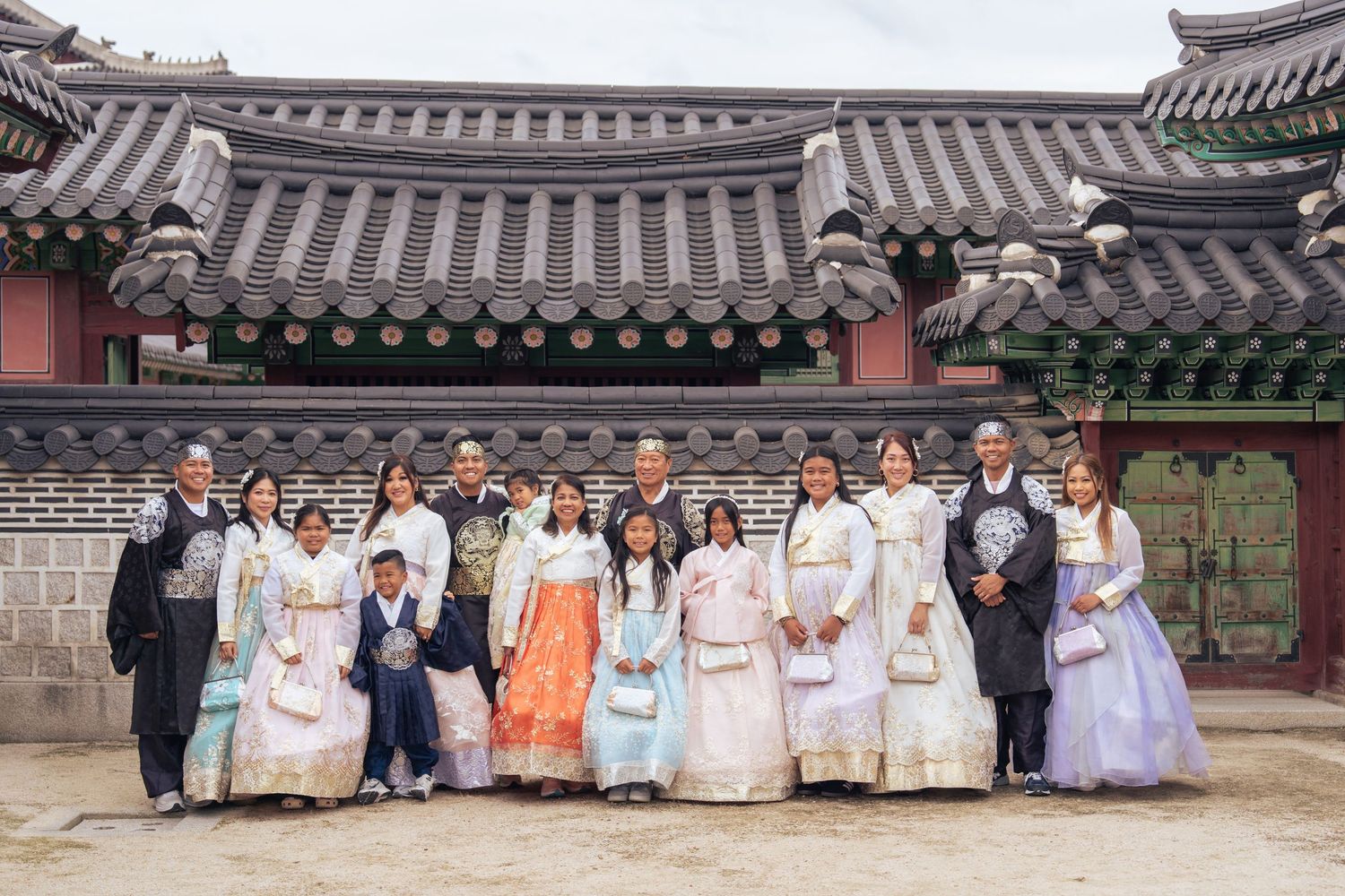 Group wearing traditional Korean hanbok clothing poses together at historic temple courtyard with traditional architecture.