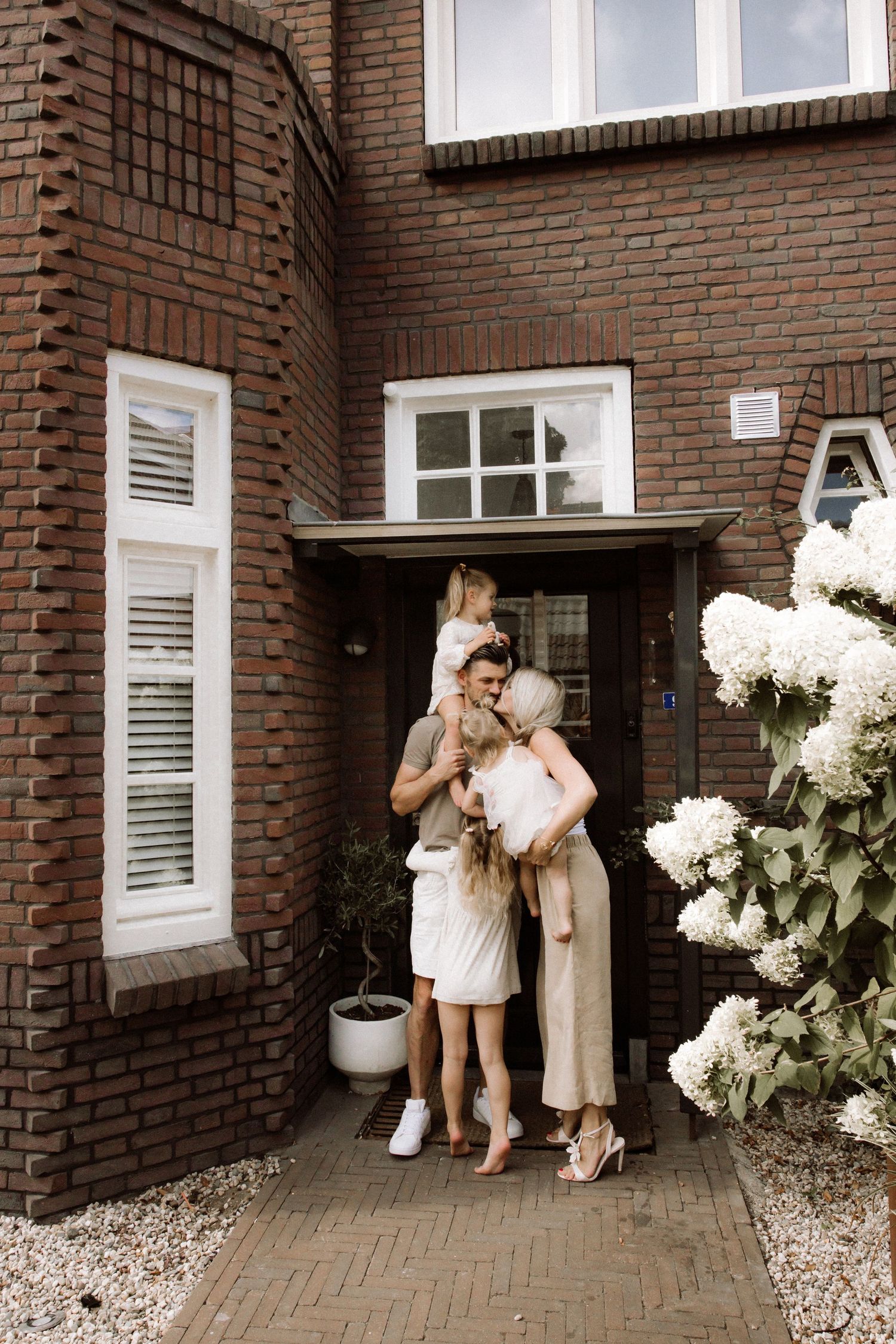Family standing together at entrance of brick house with blooming white hydrangeas.