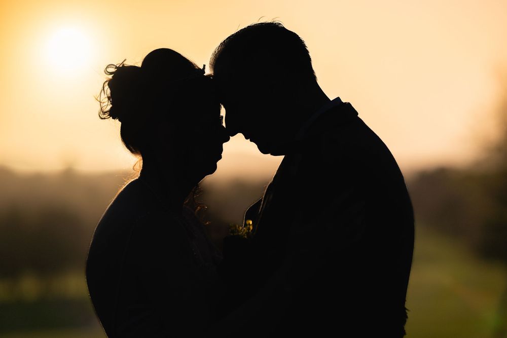 Silhouettes of a couple against a warm sunset background.