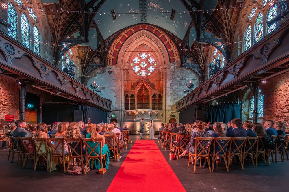 Panoramic view of wedding reception in cathedral with red carpet and cross-beam ceiling.