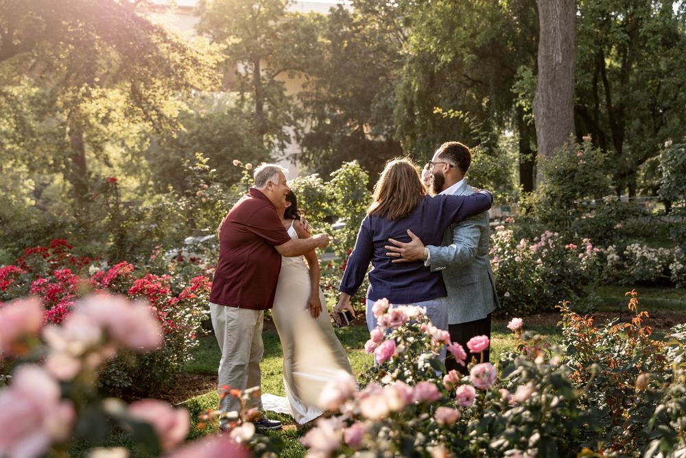 A group of people gather in a sunlit garden surrounded by blooming roses during golden hour.