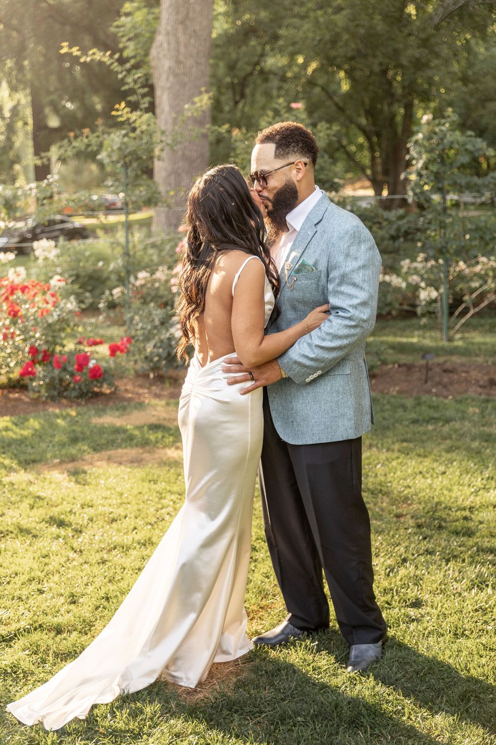 A couple shares a romantic dance together in a sunlit garden with red flowers in the background.