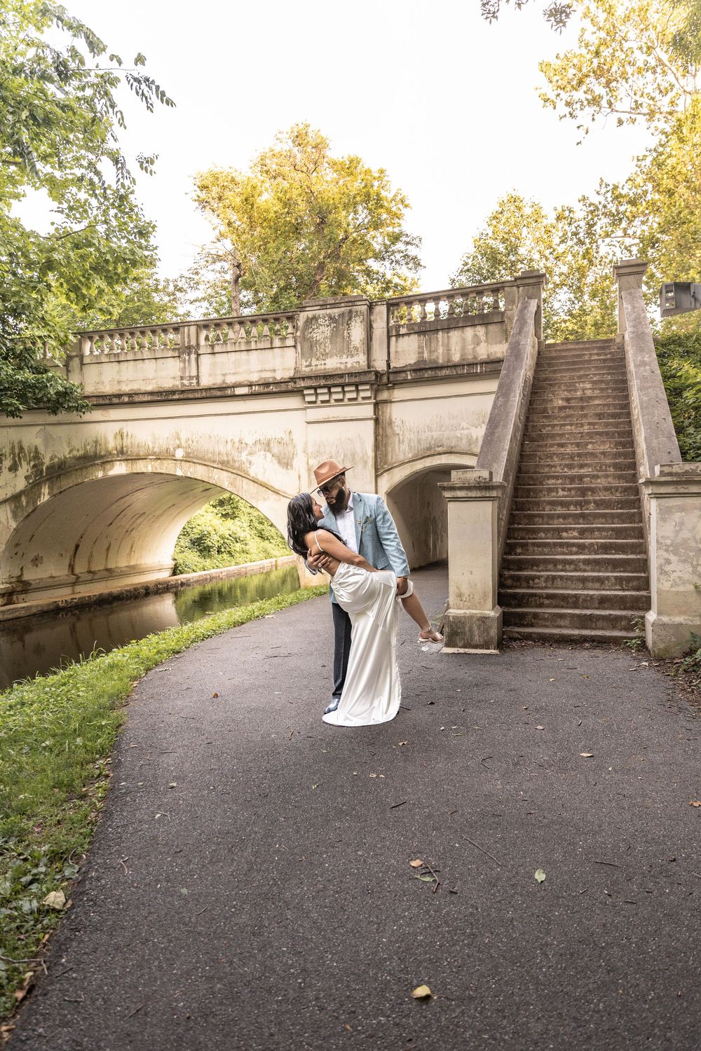 A sequence of five images showing a person performing a backbend against a stone bridge staircase in a park setting.