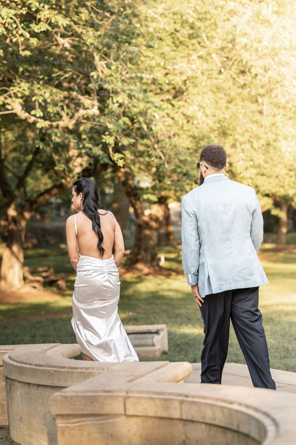 A couple sits together on a stone wall in a sunlit park during golden hour.