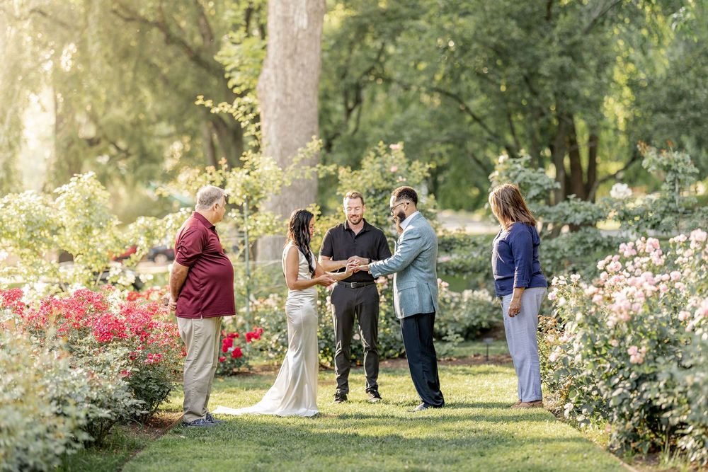 Group gathering in a blooming garden with red roses and trees in the background.